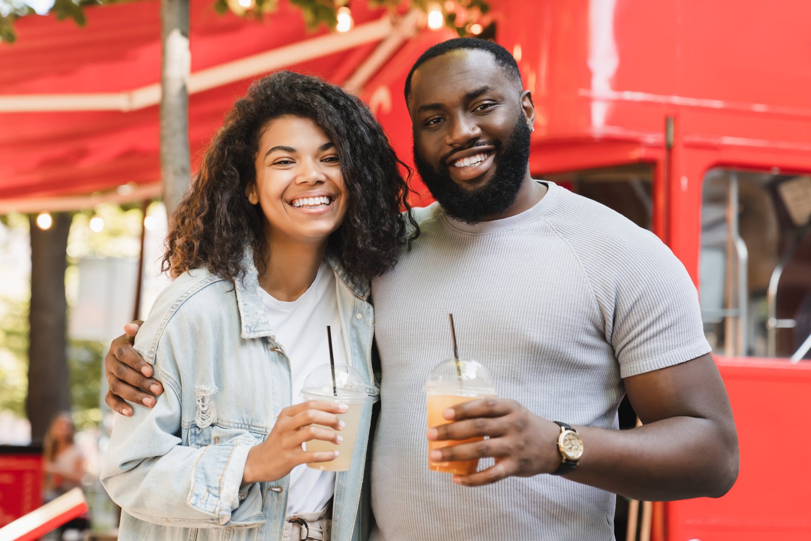 Romantic african-american young couple friends looking at the camera, embracing, walking together on date drinking juice lemonade in city park cafe outdoors. Love and relationship concept