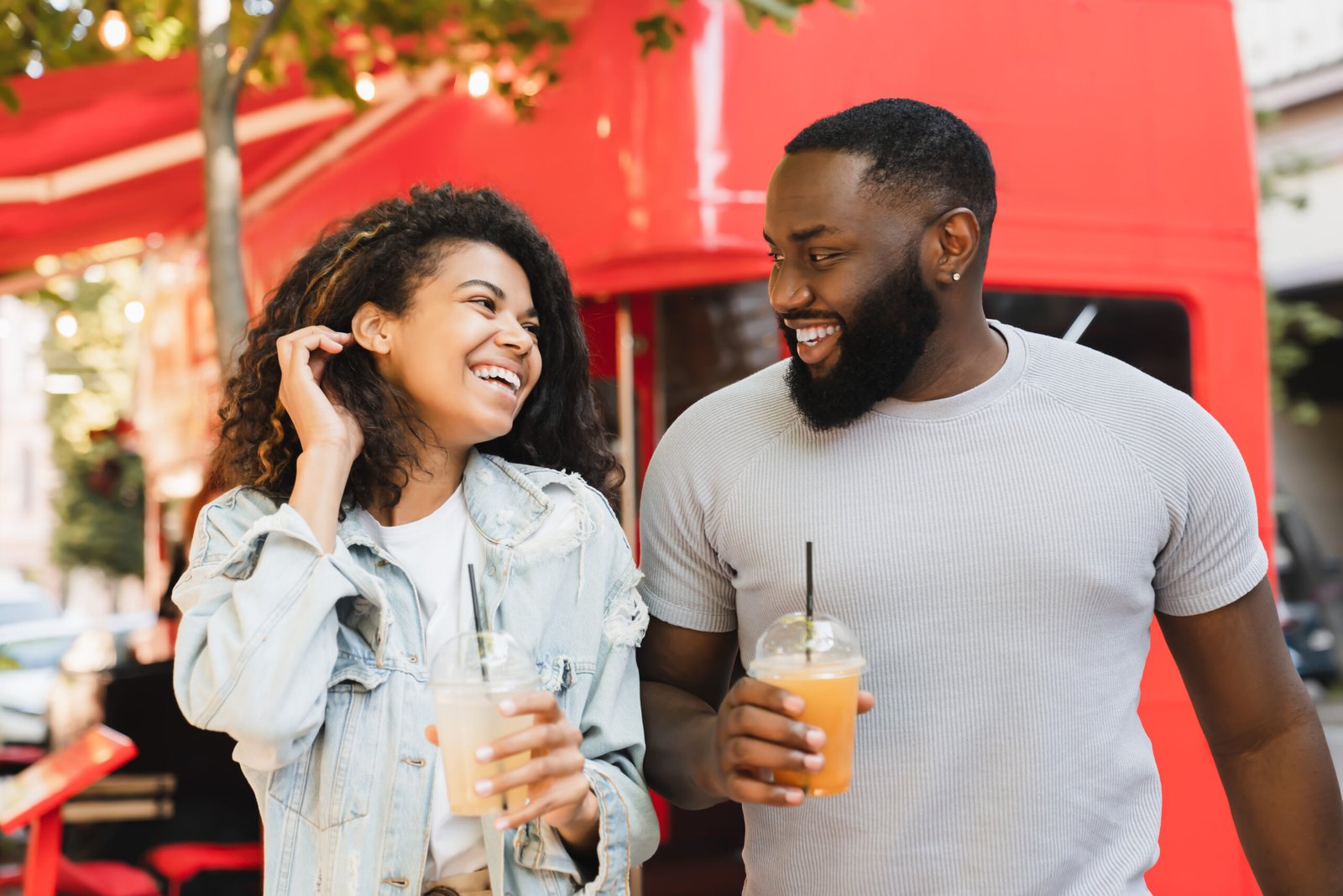 Romantic african young couple friends walking together on date drinking juice lemonade in city park cafe outdoors. Love and relationship concept